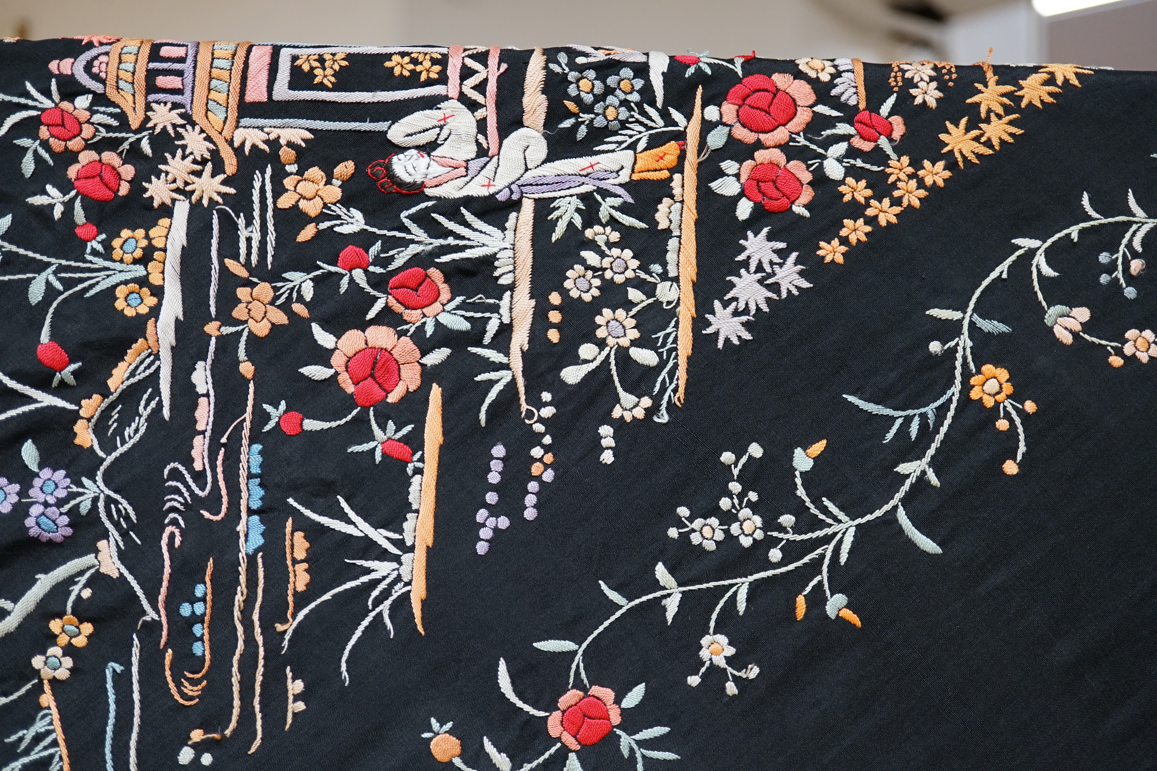 An early 20th century Chinese black silk shawl, with all over coloured floral embroidery, embroidered with multi-coloured silks and a long silk fringe, unusually the four corners are embroidered with a figurative pagoda